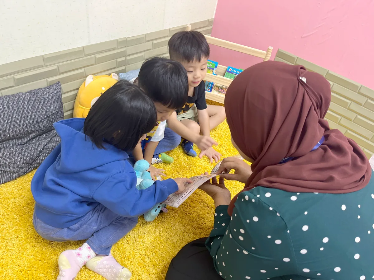 A teacher and three children leaning in to look at a storybook together