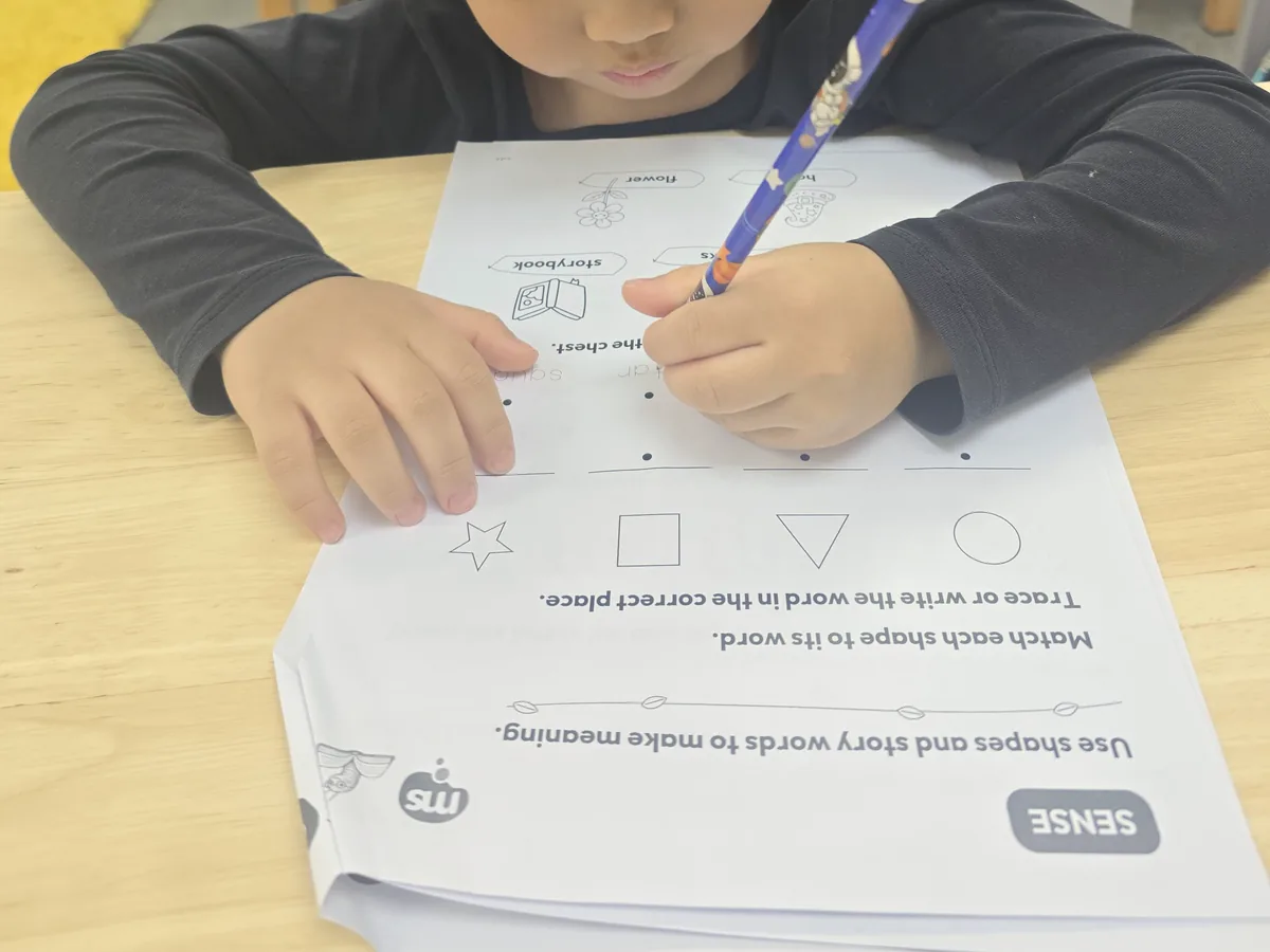 A child tracing shapes and story words on a StoryQuest worksheet