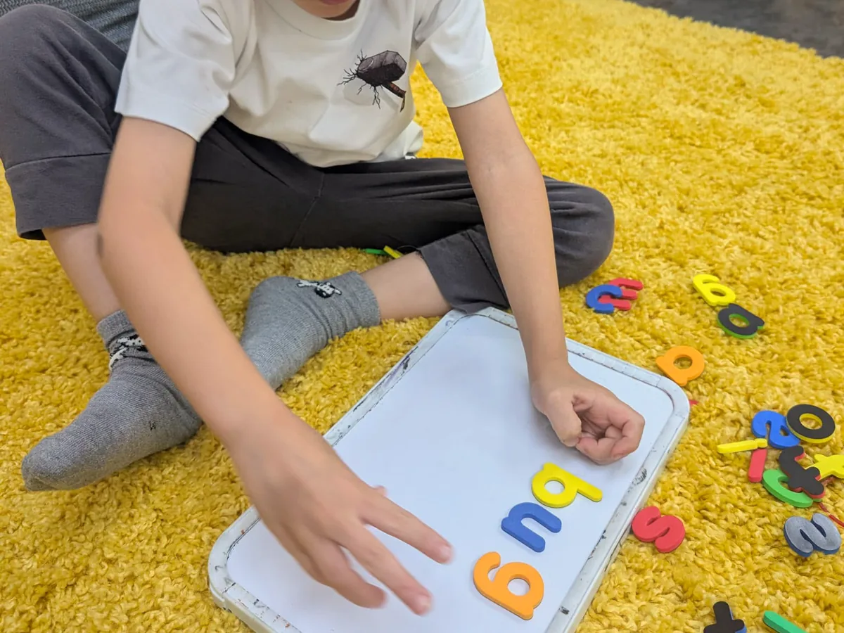 A child arranging magnetic letters to spell the word bug on a whiteboard